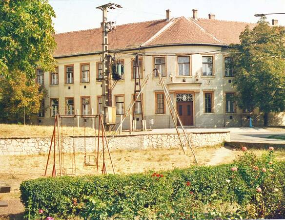 Gebäude im Hintergrund, von Bäumen gesäumt, im Vordergrund ein Spielplatz