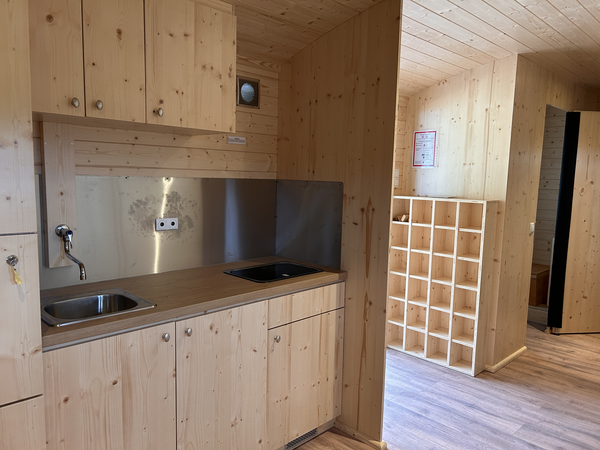 Eine kompakte Küche aus hellem Holz mit zwei Spülbecken und einem Regal im Hintergrund.