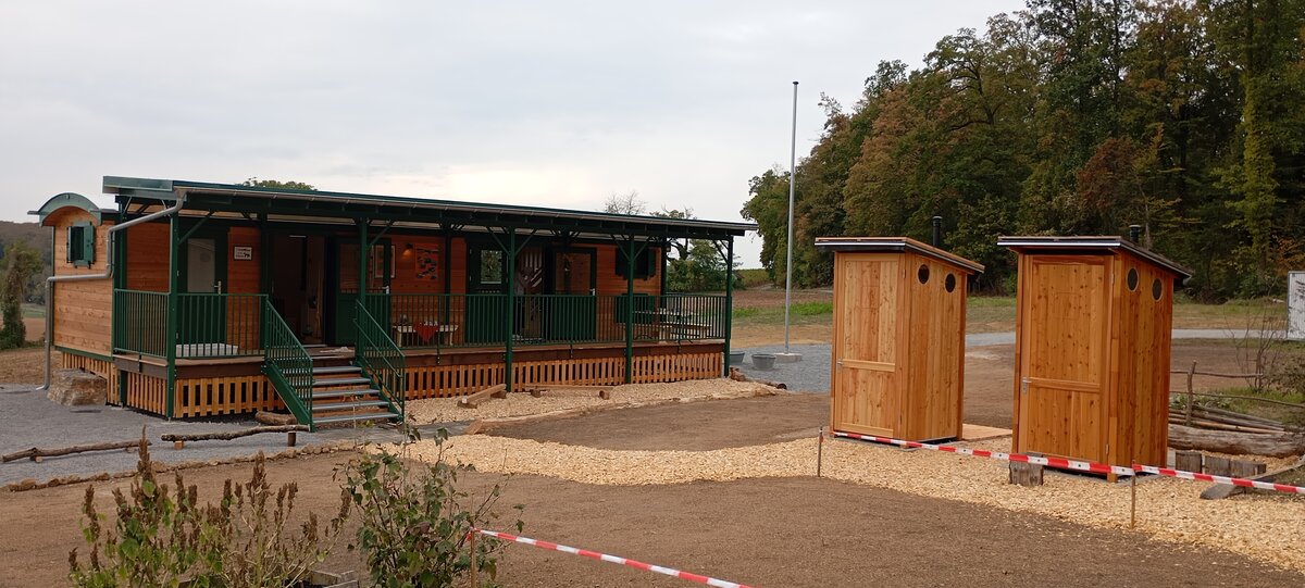 neuer Bauwagen und Zwei Toilettenhäuschen aus Holz  stehen auf frisch angelegtem Gelände