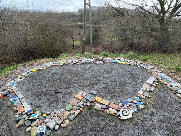 Der Buchstabe W für Walzbachtal aus bemalten bunten Steinen geformt. Außenherum ist Grünfläche und Büsche