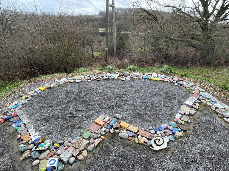 Der Buchstabe W für Walzbachtal aus bemalten bunten Steinen geformt. Außenherum ist Grünfläche und Büsche