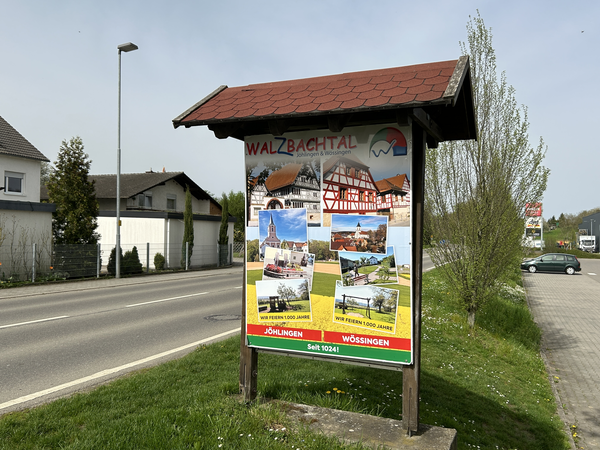 Ortstafel mit Veranstaltungshinweis zu 1.000 jährigen Jubiläum. Daneben Häuser und Fahrzeuge