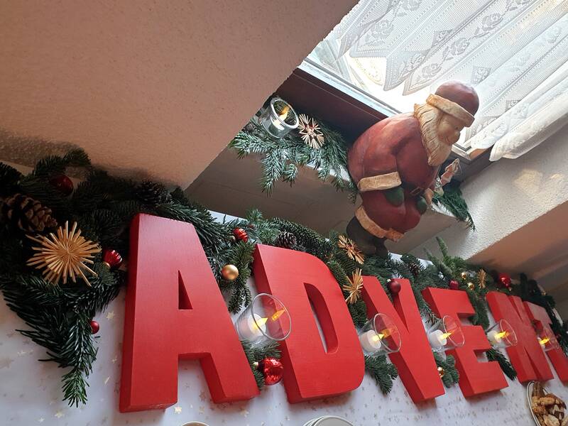 Roter Schriftzug ADVENT auf Tisch mit Tannengrün, rundliche Nikolausfigur auf Fensterbrett