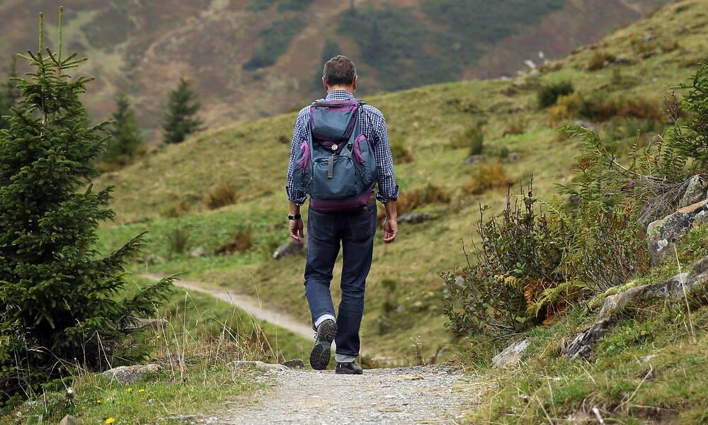 Ein von hinten zu sehender Mann wandert mit Rucksack durch hügelige Landschaft