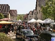 Bild vom Wössinger Straßenfest, Stände rechts und links am Straßenrand, Menschenmenge in der Mitte und Autos im Vordergrund